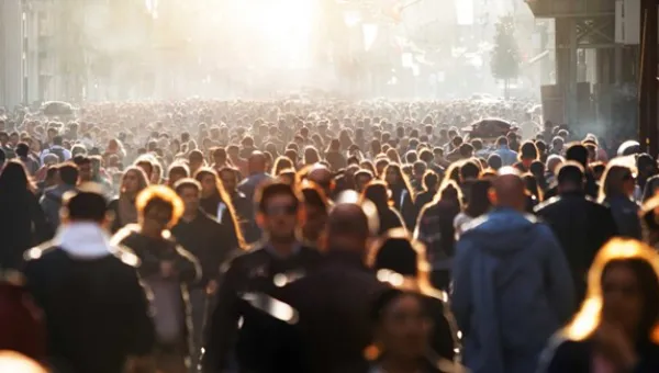 A large crowd of people stretches as far as the eye can see. A low, bright sun highlights a number of individuals who make up the crowd