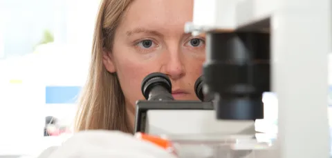 face of a woman placing a sample under a microscope