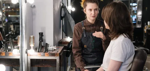 A hair stylist talking with a client in a salon