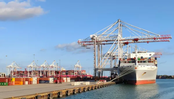 Cargo ship docked at a port with stacked containers and cranes against a clear sky