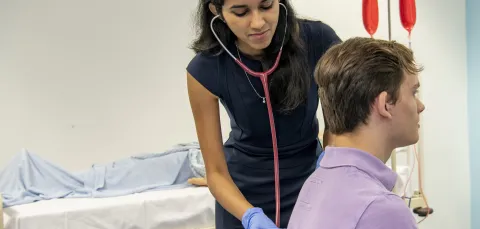 An undergraduate medicine student practices using a stethoscope on a patient in the clinical skills suite