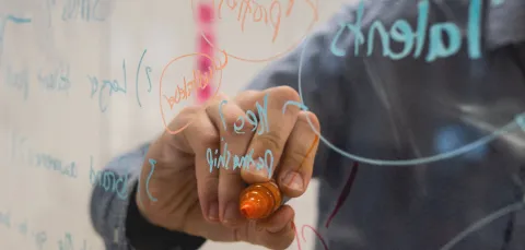 Close up of someone's hand as arm as they write in felt tip on a transparent board