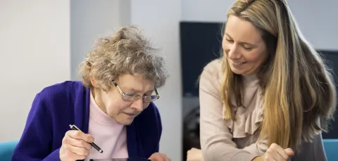 An older woman uses a tablet supported by a younger woman 