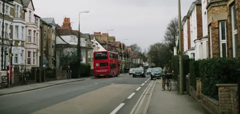 A road with a red bus, a cyclist pushing a bike, a pedestrian and cars