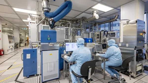 Two men in full cleanrooms uniforms are sitting at the desks working with equipment