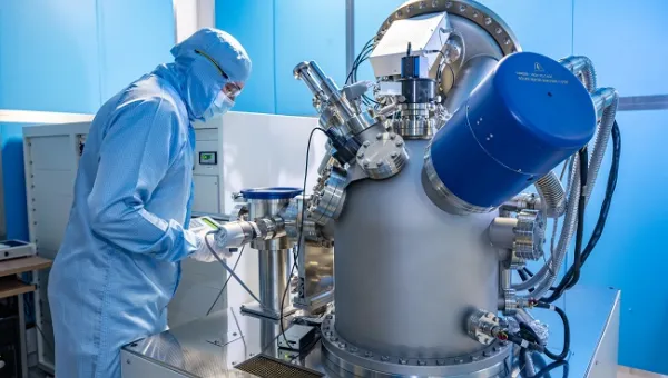 A man in full cleanroom uniform is working with equipment