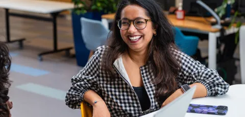 A student smiling while sat at a desk on a university campus.