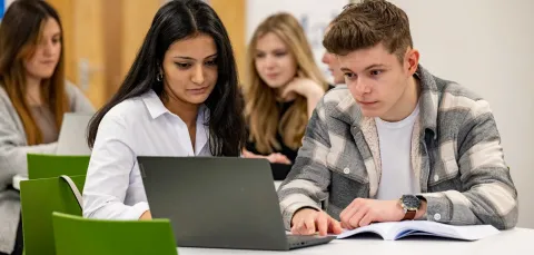 Two students at a table with a laptop