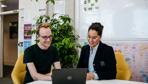 James Baker and Ammandeep K Mahal are in an office, smiling and looking at a laptop screen together.