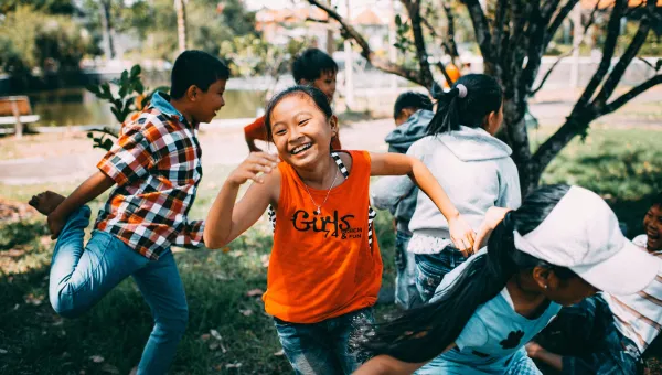 Children energetically playing outdoors, with a focus on a laughing girl in an orange shirt.