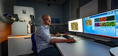 A technician works at computers displaying microscopic images, with a TESCAN electron microscope nearby.