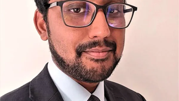 Dr Varatharaj looks out at the camera wearing a black suit and tie