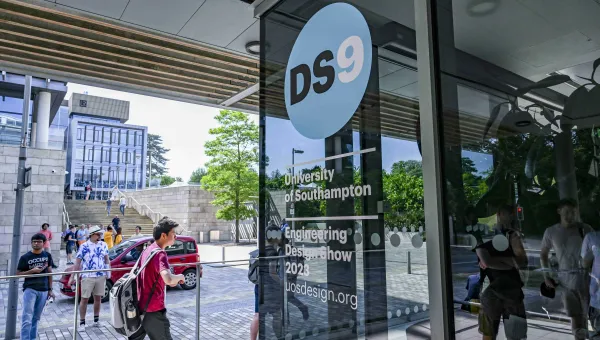 A picture of the Engineering Design Show 9 artwork "DS9" on the glass windows of an engineerin building, there are students walking past in the background.