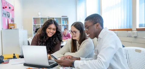 Students smiling looking at a laptop in a classroom.