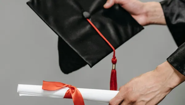 Hands proffer a graduation cap and scroll