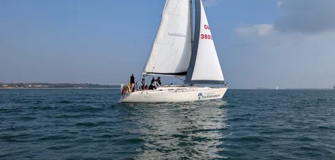 A yacht with 2 sails up and course participants sailing along the coast