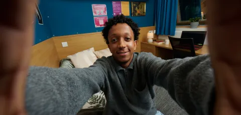 A student taking a selfie while sat on a bed in a university halls of residence.