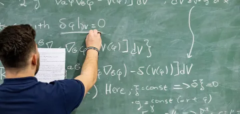 A student writing a complex mathematical equation on a blackboard