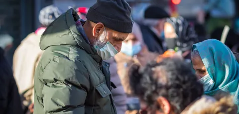 People wearing masks gather outdoors, some handing out fruit during a community food distribution.