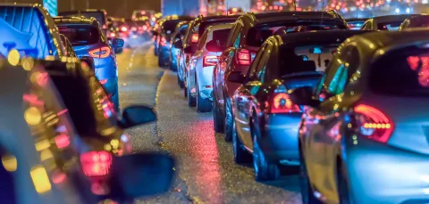 Looking along 2 rows of cars, bumper to tail with the rear lights shining. it is dark apart from the car lights.