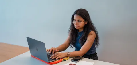 A student sat a desk with a laptop, mobile phone, passport and documents.