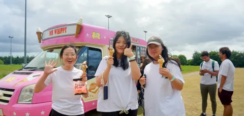 Three students stood holding ice creams, with an ice cream van in the background.