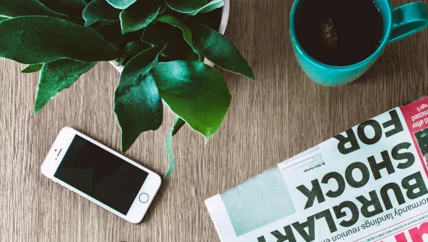 table with a mobile phone, plant, beverage in a mug and a newspaper