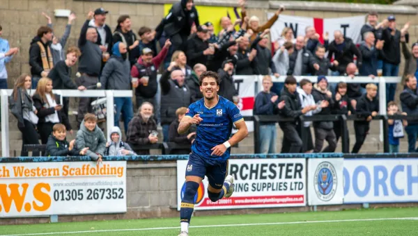 A football player running on a pitch with a cheering crowd behind.