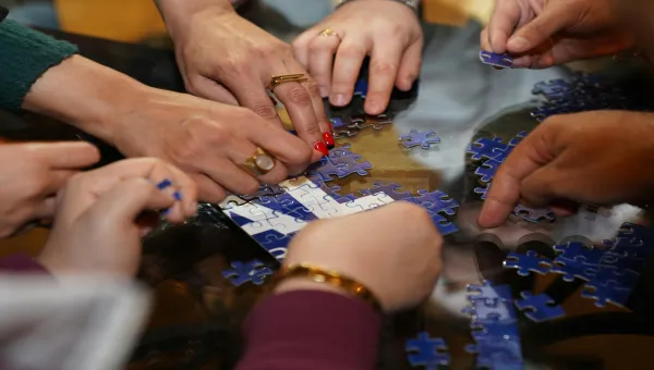 A diverse group of people collaboratively assembling a jigsaw puzzle on a table indoors
