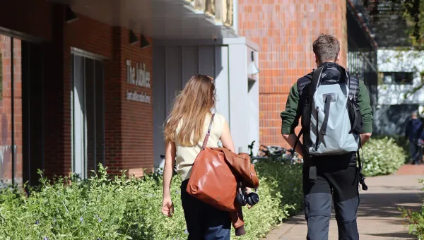 2 students walk into the Jubilee centre along a flowering hedge