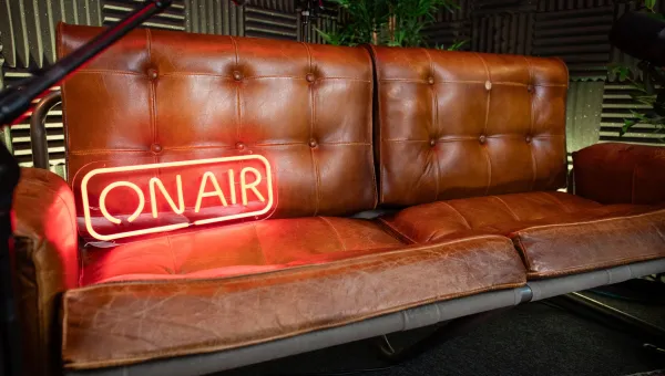 A neon "On Air" sign rests on a comfortable leather sofa surrounded by microphones and soundproofing equipment in our podcast studio