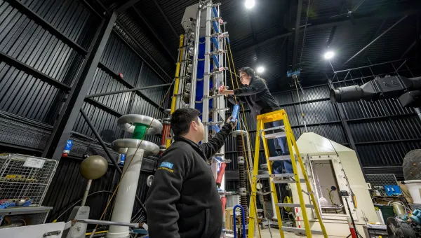 Two technicians working on a tall high-voltage testing apparatus inside the Tony Davies High Voltage Laboratory