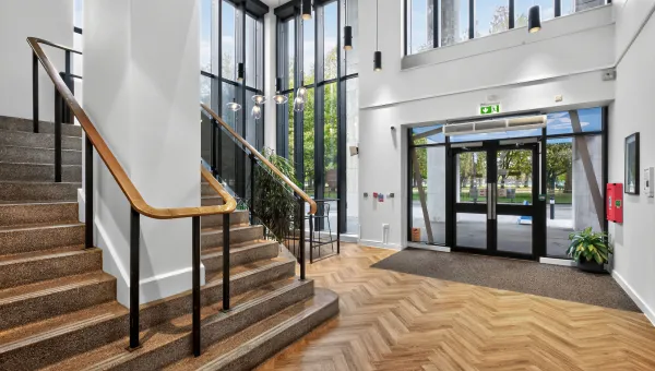 A well-lit image of the Captial House reception area. It features a large staircase and tall windows.
