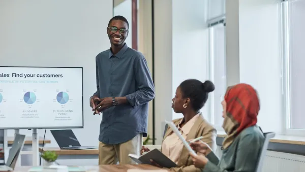 A person standing in front of a table delivers a talk to colleagues who are seated