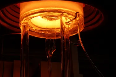 Glowing furnace with glass rods extending downward, emitting orange light.