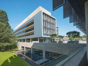 Exterior shot of modern building, surrounded by grass and trees, on a sunny day.