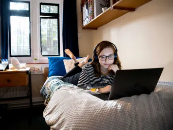 Student laying on bed, working on laptop.