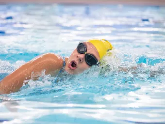 A swimmer in goggles and yellow cap cuts through the water while swimming in a pool.