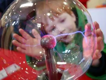 Young child with hands placed on glass electricity ball