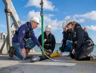 Several students at sea, crouching around an autonomous marine drone.