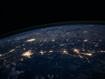 The darkened surface of the Earth at night, as seen from space, with lit-up cities visible.