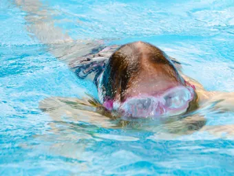 Close up of a child in a swimming pool, their goggles features peeping above the water