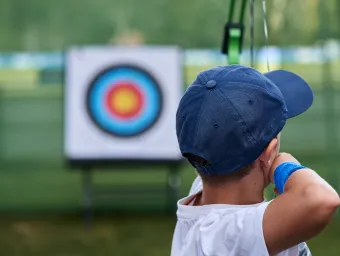 Close up of a child, seen from behind, about to shoot an arrow at an archery target.
