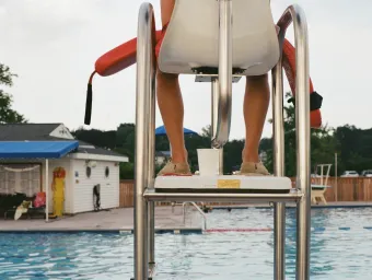 A lifeguard, seen from behind, keeps watch over on an outdoor swimming pool