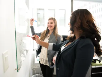 Two women in an office writing on a whiteboard