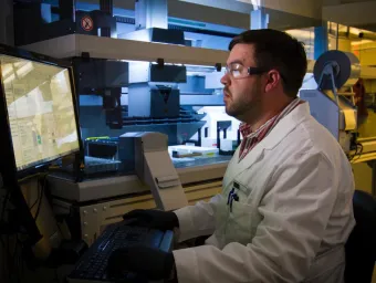 A biological sciences researcher in a white lab coat, works at a computer in a laboratory