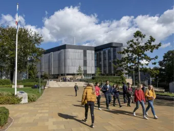 Students walk on a sunny campus with modern buildings and greenery