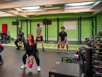 People in a gym lifting a kettlebell from a squatting position