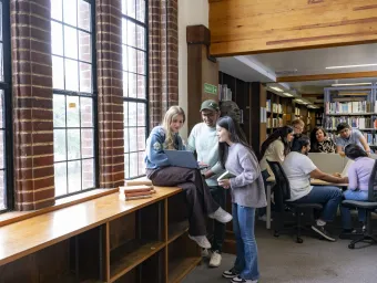 Two groups of students in the Hartley library. I group looking at a laptop and the other talking around a table.