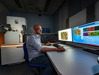 A technician works at computers displaying microscopic images, with a TESCAN electron microscope nearby.